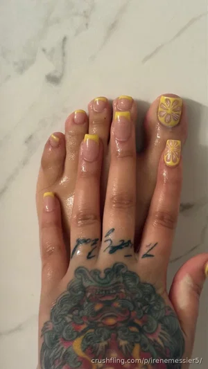 Hand with colorful tattoo and yellow floral nail art on marble surface.