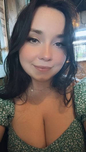 Woman with dark hair in green floral top, smiling, indoor setting.