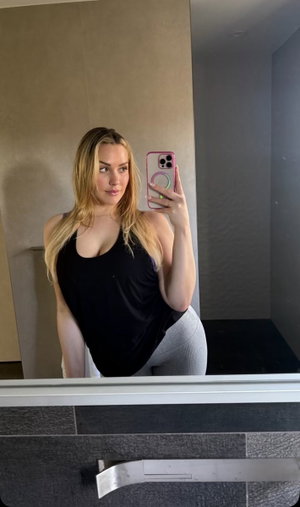 Blonde woman in black tank top and gray leggings in bathroom mirror selfie.