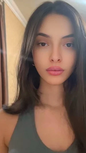 Woman with long dark hair wearing olive green tank top indoors.
