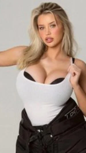 Blonde woman in white top and black pants posing indoors.