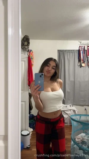 Woman in white crop top and red plaid pants takes mirror selfie in bedroom.