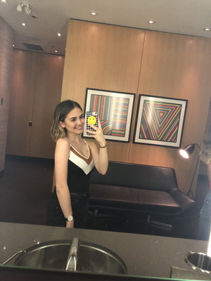 Woman in black and white top taking mirror selfie in modern room with artwork.