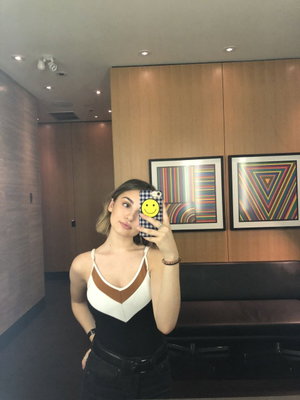 Woman in black and white top, dark pants, taking mirror selfie in modern indoor space.