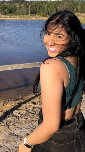Woman with long dark hair in green top by a lake.