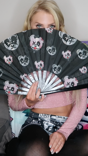 Blonde woman holding patterned fan in pink crop top indoors.