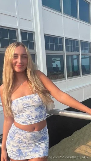 Blonde woman in blue and white patterned two-piece outfit standing outdoors near a white building.