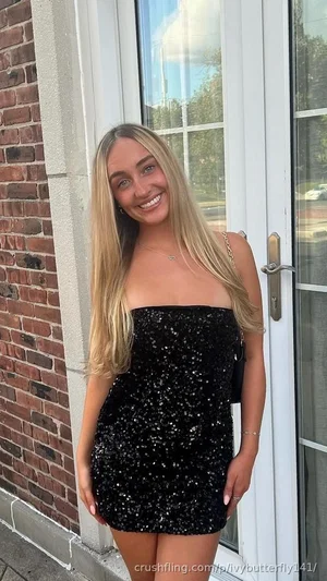 Woman with long blonde hair in a black sequined strapless mini dress standing by a brick wall and