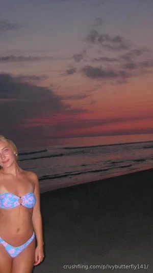 Woman in pink and blue bikini standing on beach at sunset.