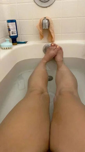 Person with bare legs and feet in a bathtub, legs crossed at ankles, indoor bathroom setting.