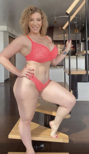 Curvy woman in red lace lingerie on indoor stairs.