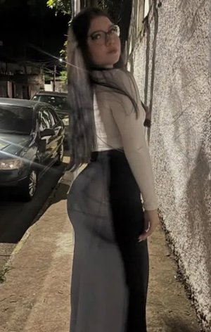 Woman with glasses and long hair in sheer top outdoors at night.