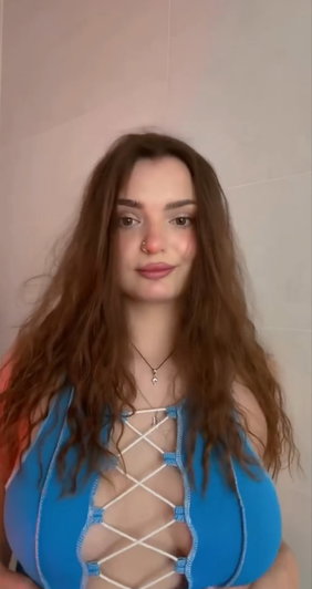 Woman with long brown hair wearing blue lace-up top, indoors.