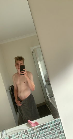 Young man taking mirror selfie in bathroom with towel.