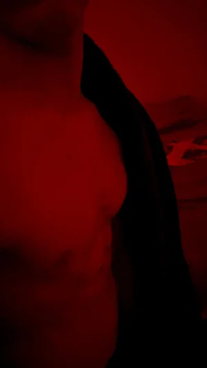 Shirtless man in red lighting, partial torso visible, dark background.