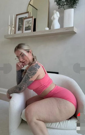 Woman with tattoos in pink athletic wear sitting on white chair indoors.