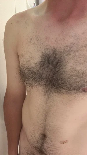 Shirtless man with chest hair standing indoors, torso visible.