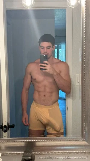 Shirtless man in yellow underwear taking mirror selfie in bathroom.