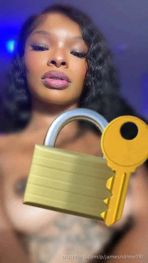 Woman with curly hair and tattoos, topless, holding a padlock and key graphic.