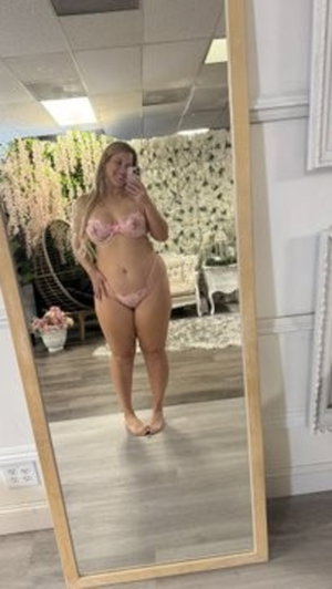 Woman in pink lingerie taking mirror selfie in decorated room.
