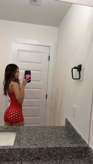 Woman in red polka dot outfit taking bathroom mirror selfie.