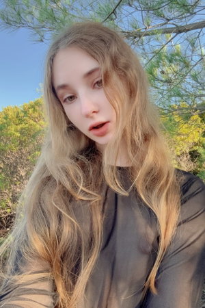 Woman with long blonde hair in sheer top outdoors.