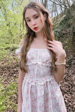 Woman with long brown hair in floral dress outdoors in forest.