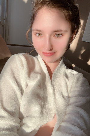 Woman in white robe, sitting indoors, soft lighting, relaxed expression.