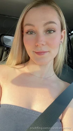 Blonde woman in a gray strapless top sitting in a car, wearing a seatbelt.