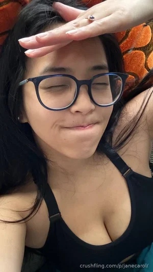 Woman with dark hair and glasses wearing a black tank top, lying down with hand on forehead.