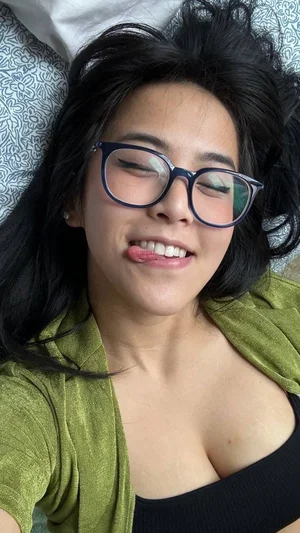 Woman with dark hair and glasses lying down, wearing a green cardigan over a black top.