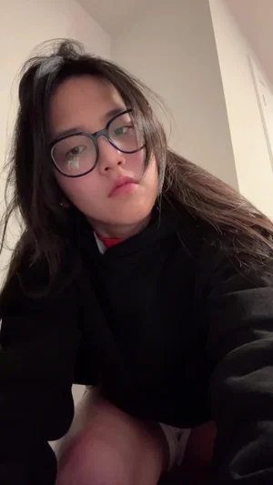 Woman with long dark hair and glasses wearing black top, indoors.
