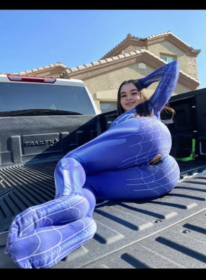 Woman in blue bodysuit posing in truck bed outdoors.