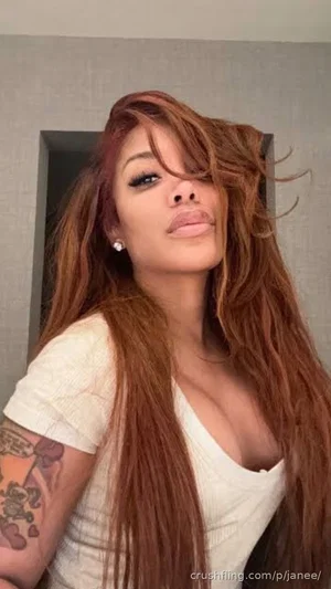 Woman with long brown hair, wearing white top, tattoo on arm, indoors.