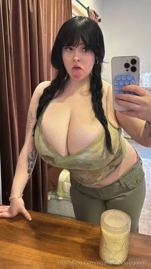 Woman with black braids in olive top and pants, making playful face in mirror selfie.