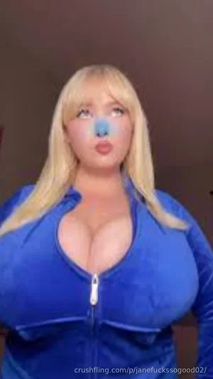 Woman with blonde hair in blue zip-up top, indoors, facing camera.