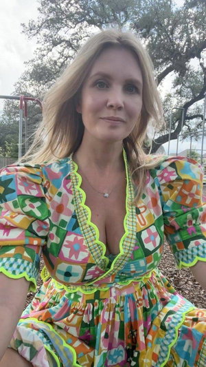 Blonde woman in colorful dress taking outdoor selfie.