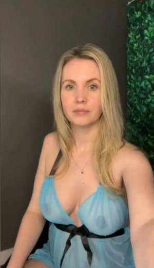 Blonde woman in sheer blue lingerie taking indoor selfie.