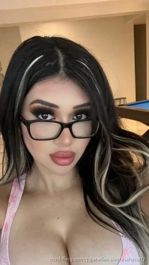 Woman with long dark hair and glasses wearing a pink top, indoors.