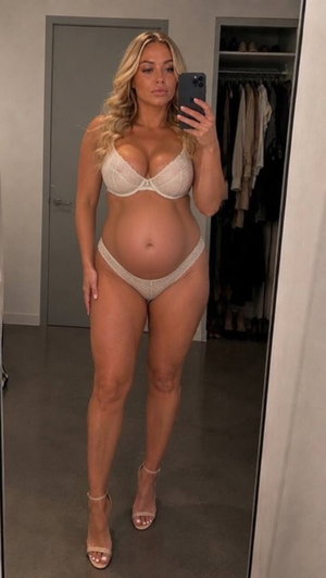 Woman with blonde hair in white lingerie taking mirror selfie in bedroom.