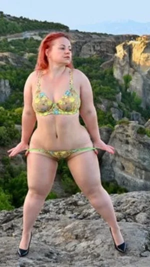 Woman in floral bikini and heels standing on rocky cliff outdoors.