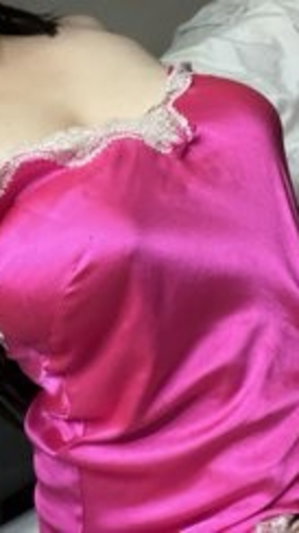 Woman in pink satin lingerie with lace trim, lying on bed.