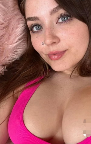Woman with brown hair and blue eyes wearing pink top, lying on pink furry surface.