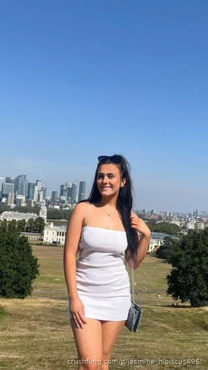 Woman in white dress standing outdoors with city skyline in background.