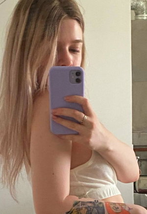 Woman with long blonde hair in white crop top and patterned shorts taking mirror selfie indoors.