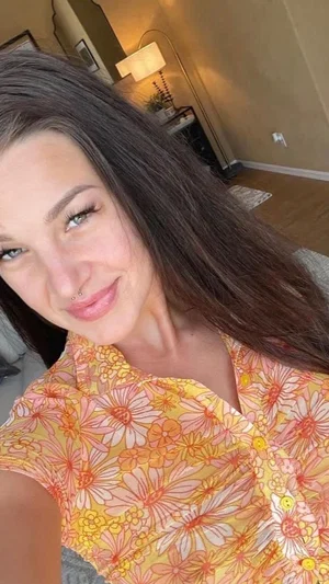 Woman with long dark hair in floral shirt, smiling in indoor setting.