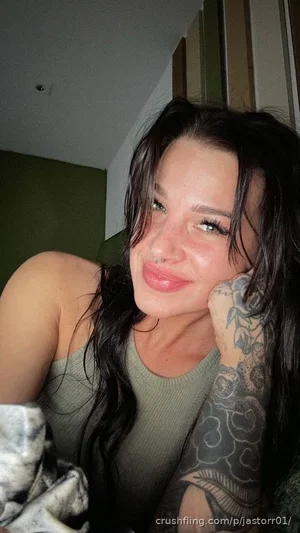 Woman with long dark hair and arm tattoos, wearing a green tank top, indoors.
