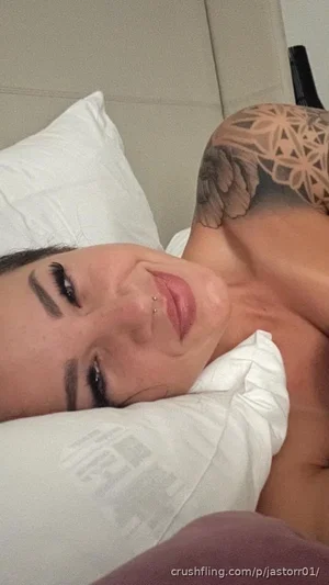 Woman with tattooed shoulder lying on white pillows in a bedroom.