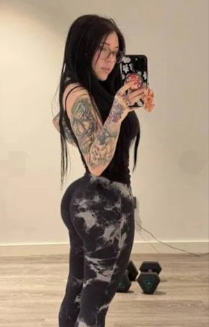 Tattooed woman with long dark hair taking selfie indoors.