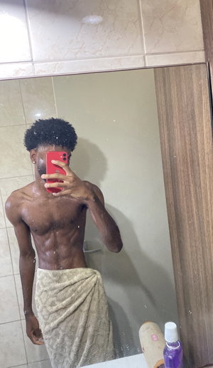 Shirtless man with towel wrapped around waist, taking mirror selfie in bathroom.
